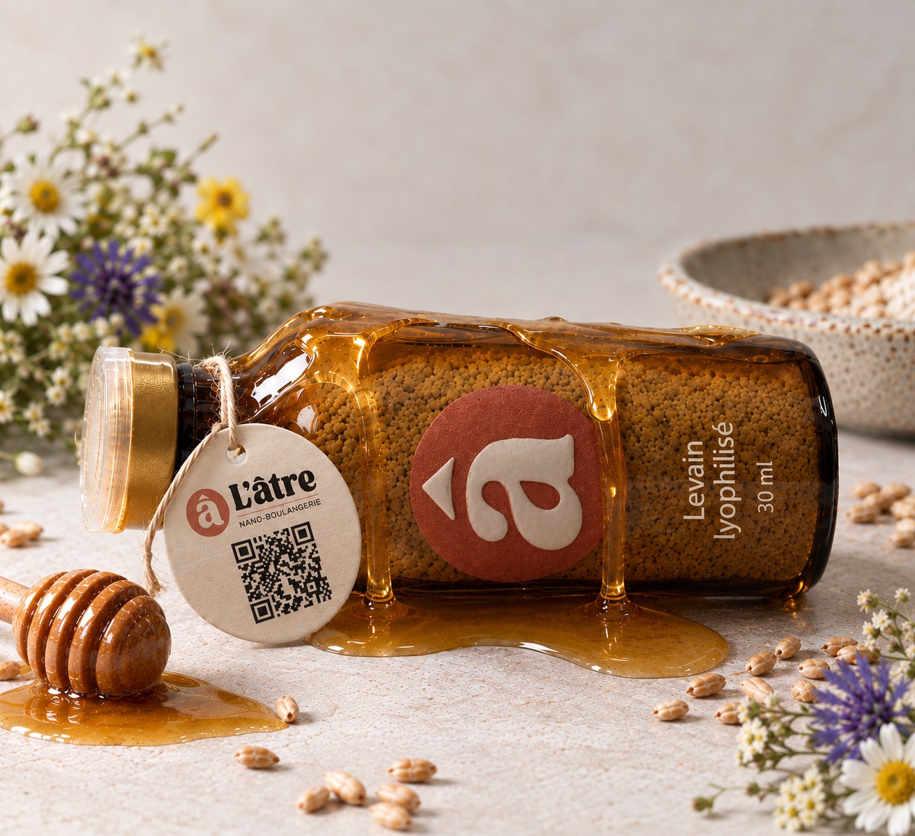 Flacon de levain lyophilisé L’âtre allongé, miel doré coulé sur la bouteille et fleurs sauvages autour